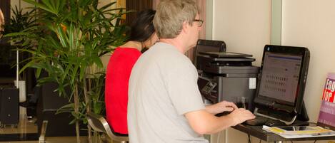 A man using a laptop at a desk with a computer monitor, a potted plant, and a book on the table.