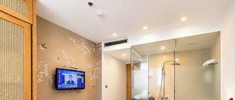 Habitación de hotel con una cama, un televisor fijado a la pared, ducha con cerramiento de vidrio y un separador de madera con diseño perforado.