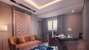 Una habitación de hotel moderna con un cabecero capitonado, un sofá, una mesa de comedor con sillas y vistas por la ventana.