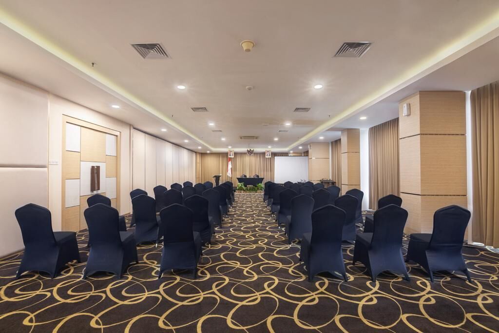 A conference room with rows of chairs, a stage, and a carpeted floor.