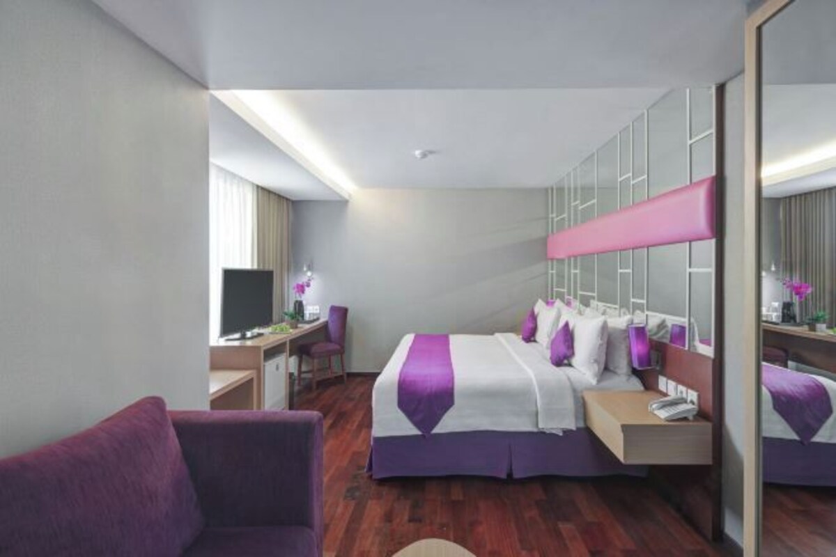 Una habitación de hotel con cama, escritorio, silla, televisor y espejo.