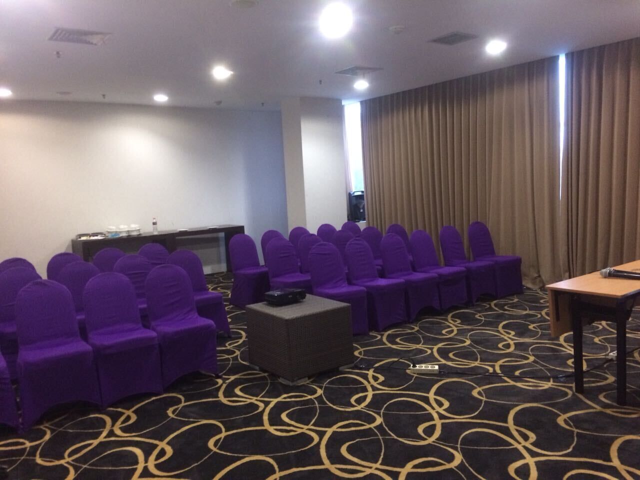 A conference room with rows of purple chairs, a small table, and a carpeted floor.