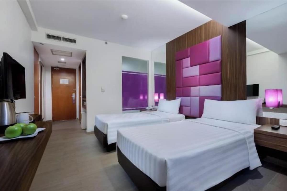 Habitación de hotel con dos camas, cabecero de madera, televisor de pantalla plana y una pequeña mesa con manzanas.