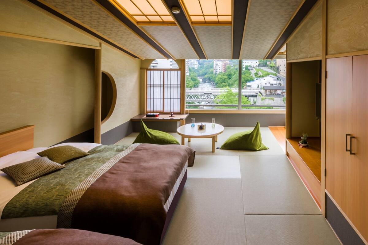 A hotel room with a bed, a small table, a sofa, and a view of the city.