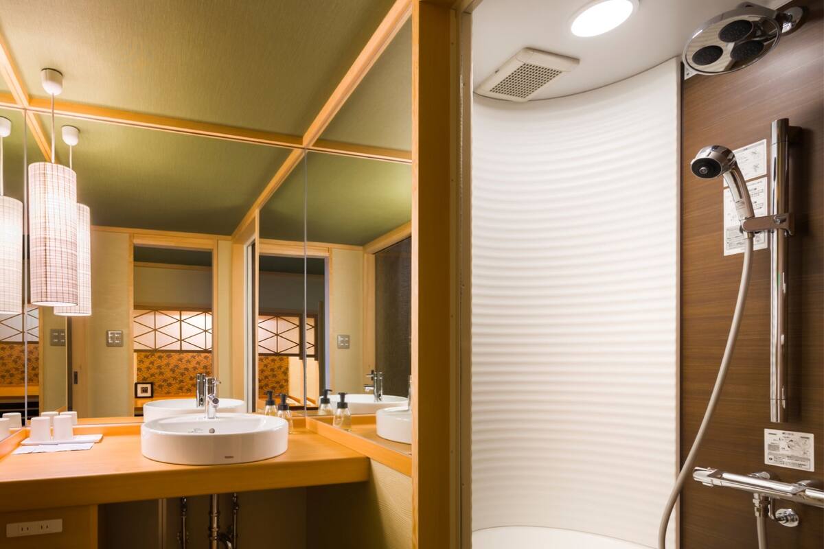 A modern bathroom with a wooden vanity, two sinks, a shower with a handheld showerhead, and a mirror.