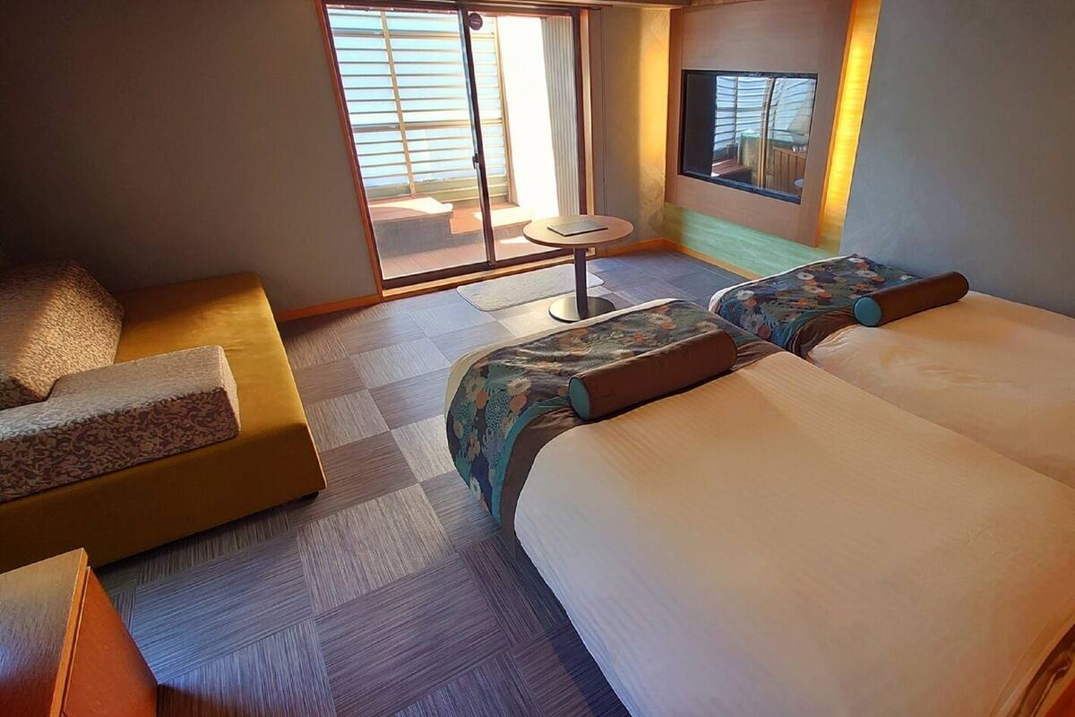 A hotel room with two beds, a sofa, a small table, and a window with a view.