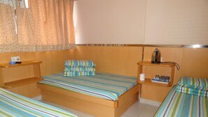 Quarto de hotel com uma cama grande, duas camas menores, uma mesinha de cabeceira com chaleira e um pequeno armário com amenities.