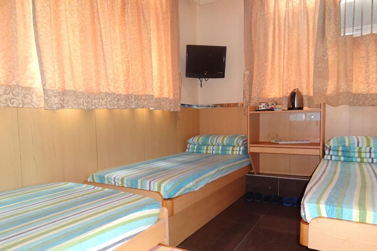 A room with two single beds, a TV mounted on the wall, a small desk with a kettle, and a sink.