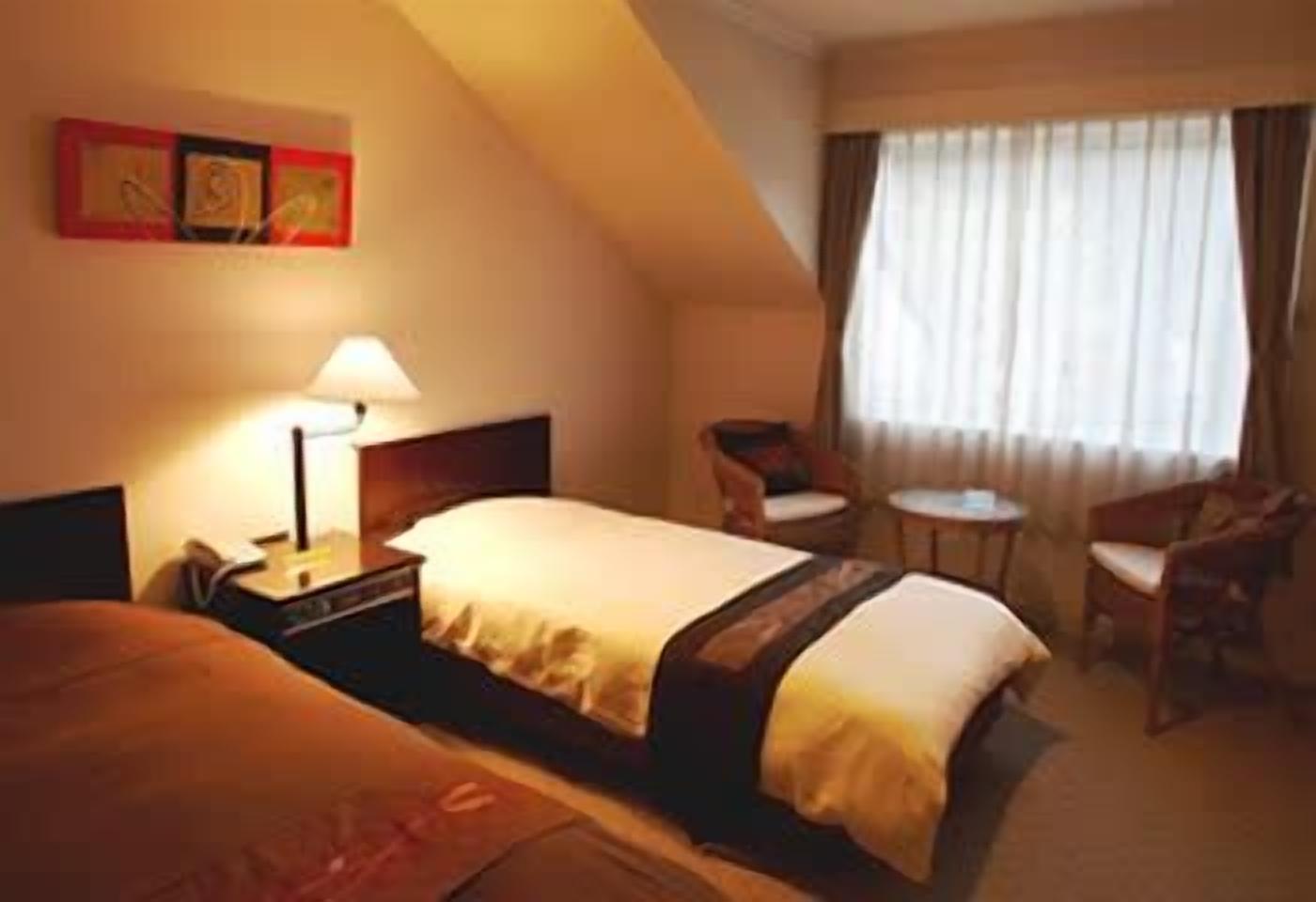 Une chambre d’hôtel comprenant un lit, une table de chevet, une lampe, une chaise et une petite table.