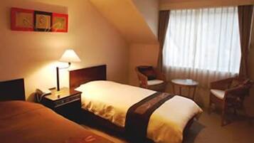 Une chambre d’hôtel comprenant un lit, une table de chevet, une lampe, une chaise et une petite table.