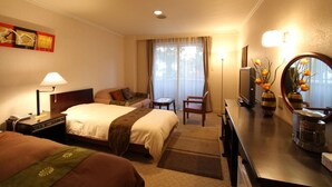 Habitación de hotel con dos camas, un escritorio con computadora, una silla, un televisor y un ventanal grande con cortinas.