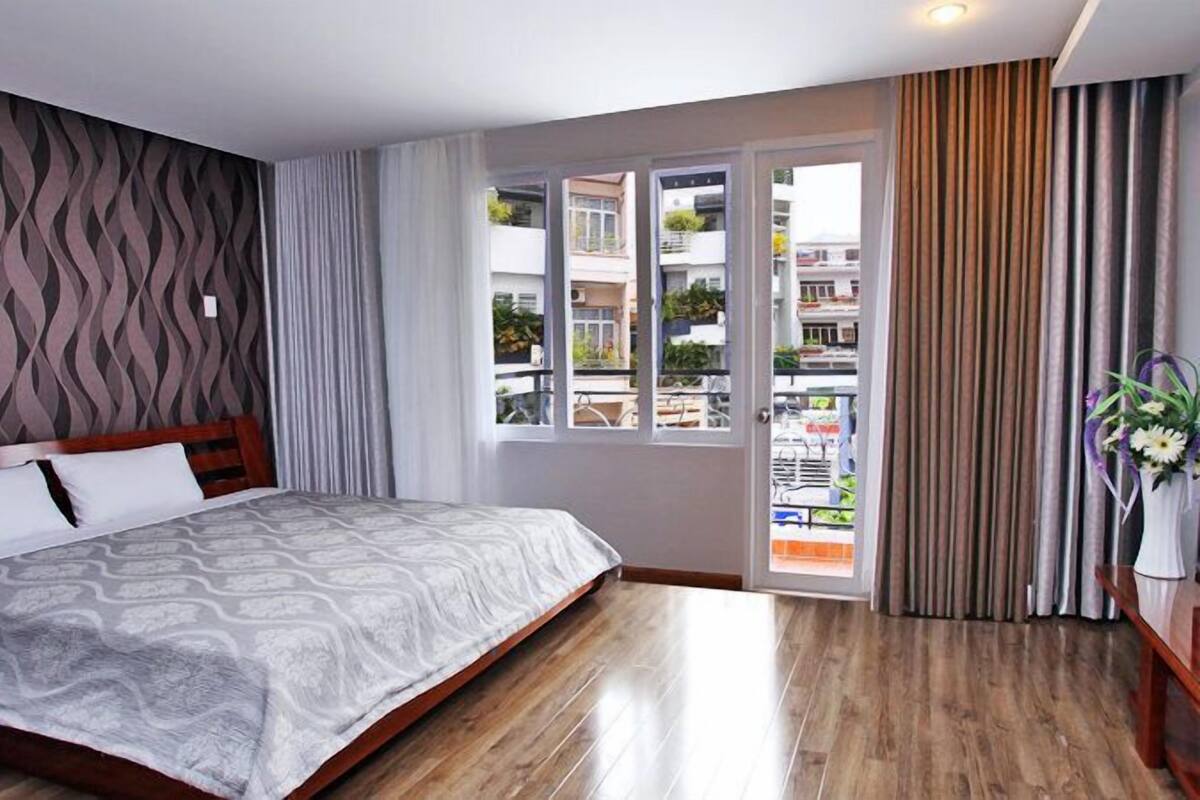 A hotel room with a bed, a window with a view of buildings, and a curtain.