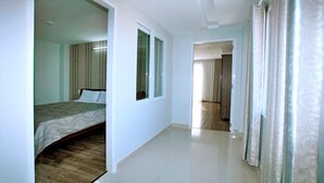 A hotel room with a bed, a window, and a door leading to another room. - White Swan Apartment (Nha Trang)