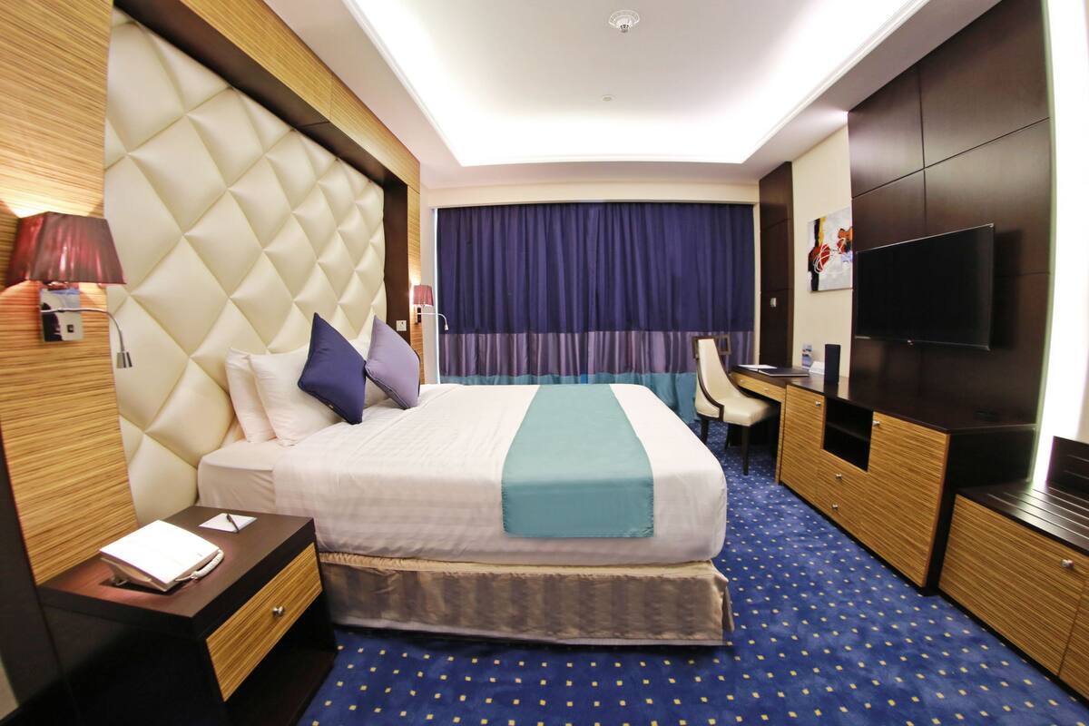 A hotel room with a large bed, a desk, a TV, and a bathroom.
