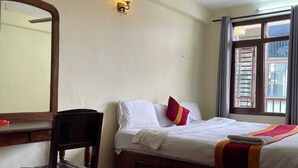 Een kamer met een bed, een bureau, een stoel, een plafondventilator en een raam met jaloezieën.