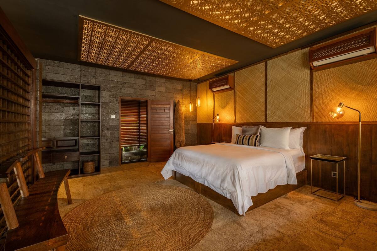 A bedroom with a large bed, wooden furniture, a stone wall, and a ceiling with a patterned design.