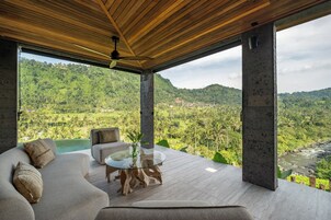 Une chambre moderne avec une table en verre, un canapé et une vue sur une vallée verdoyante.