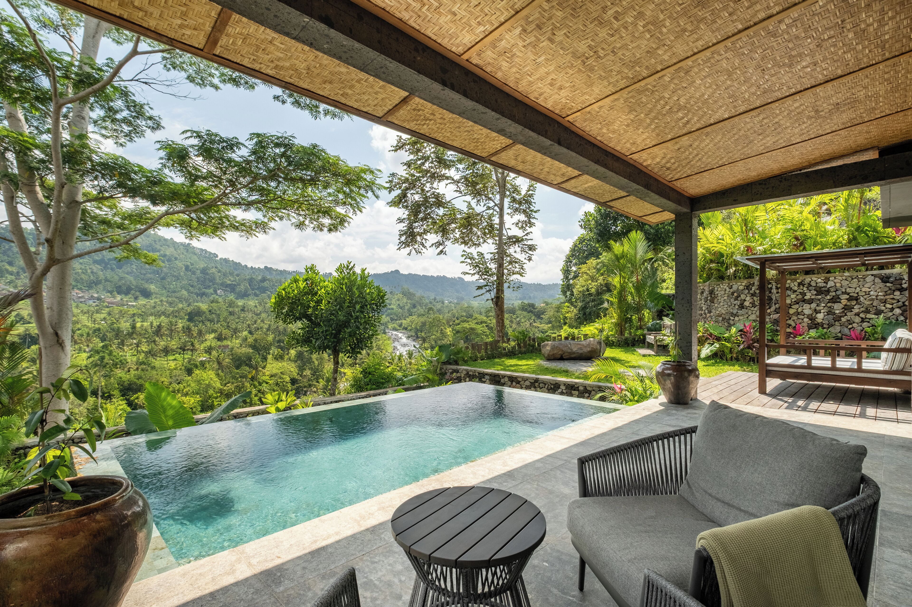 A pool area with a view of a mountainous landscape, outdoor seating, and a stone wall.