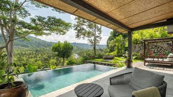 A pool area with a view of a mountainous landscape, outdoor seating, and a stone wall.