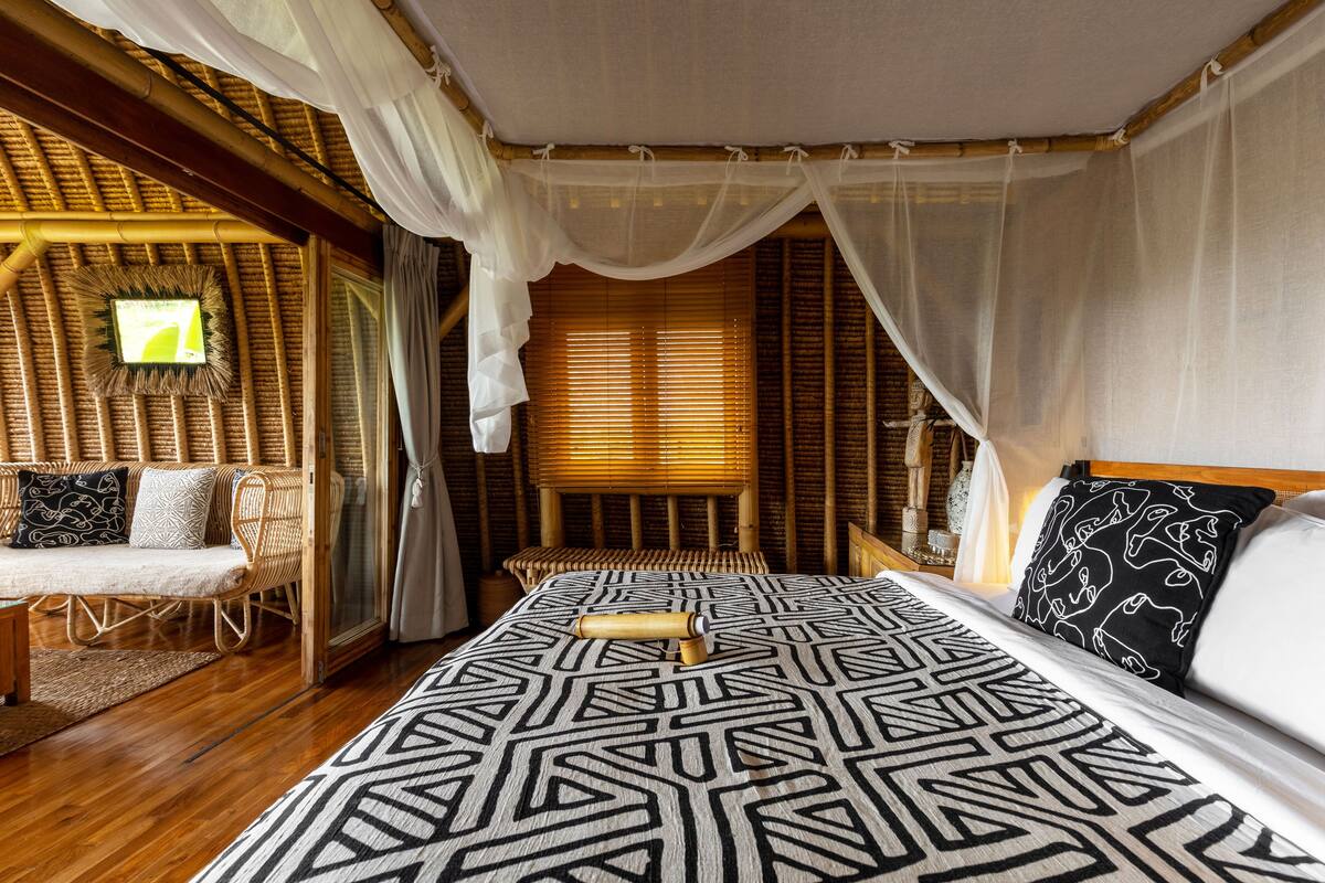 A room with a bed, a wicker sofa, and a wooden floor.