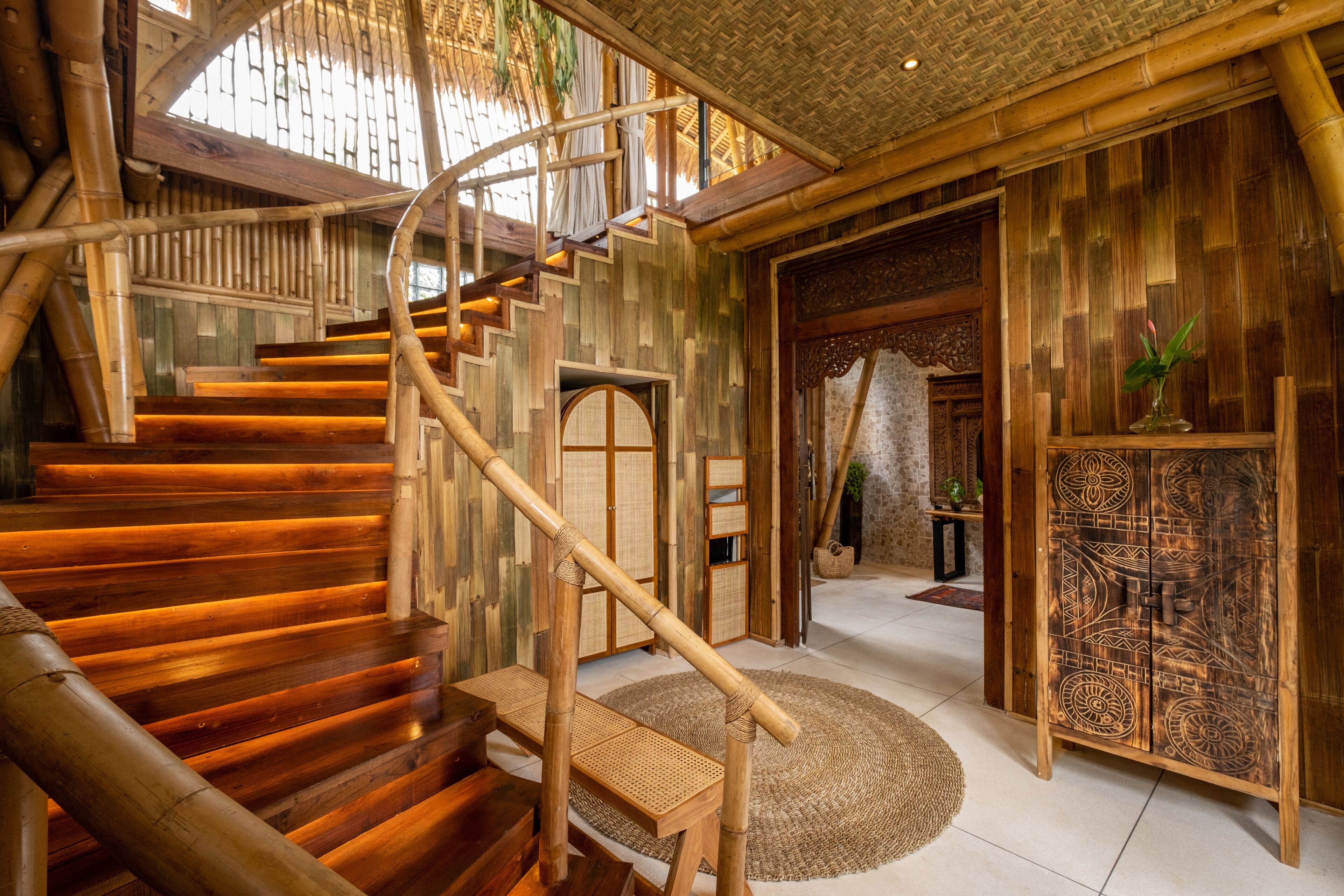 Una escalera de madera con diseño en espiral que conduce a una habitación con decoración tradicional y un gran armario de madera.