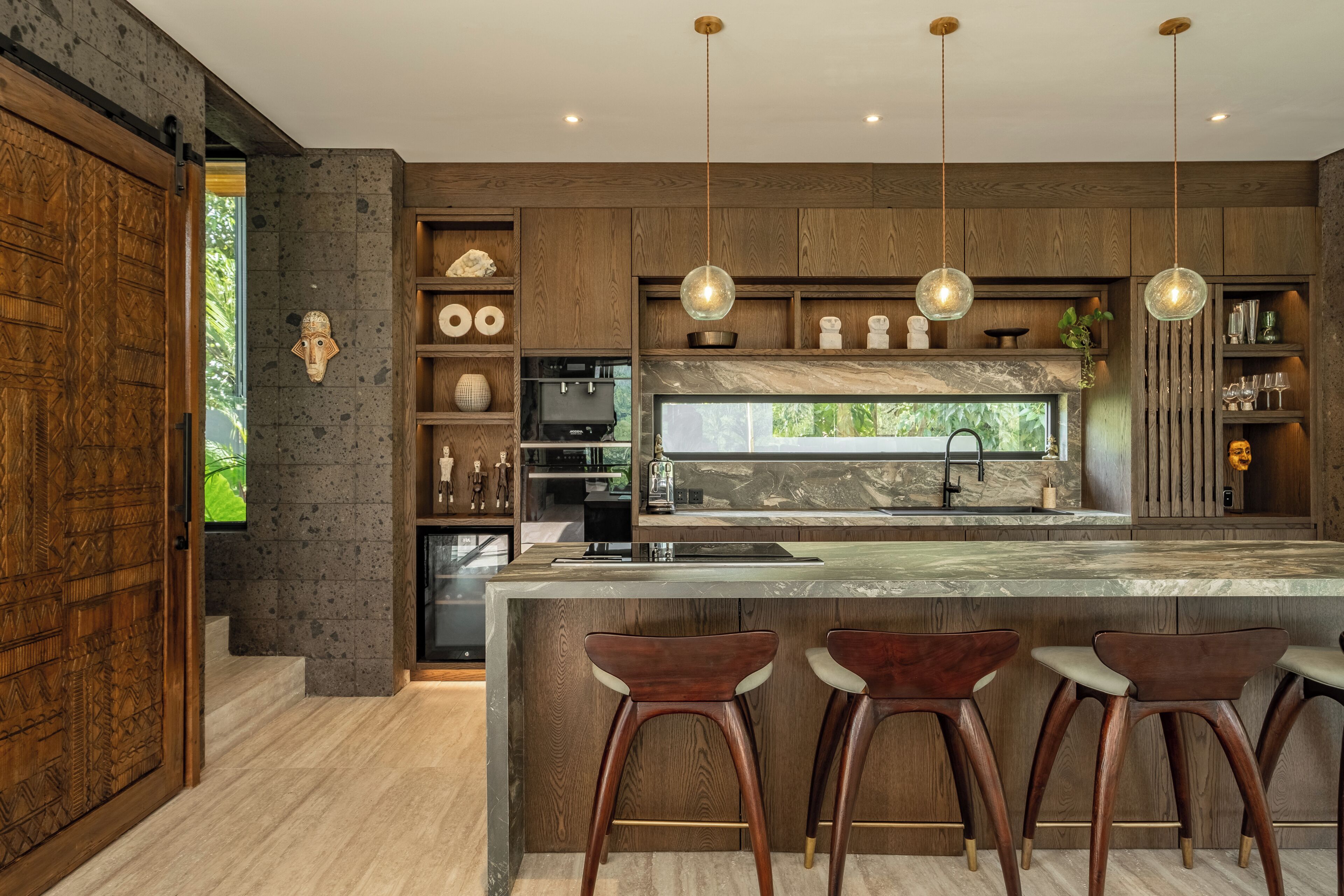 A modern kitchen with a large island, bar stools, pendant lights, and a stone backsplash.