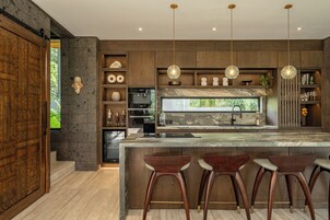 A modern kitchen with a large island, bar stools, pendant lights, and a stone backsplash.