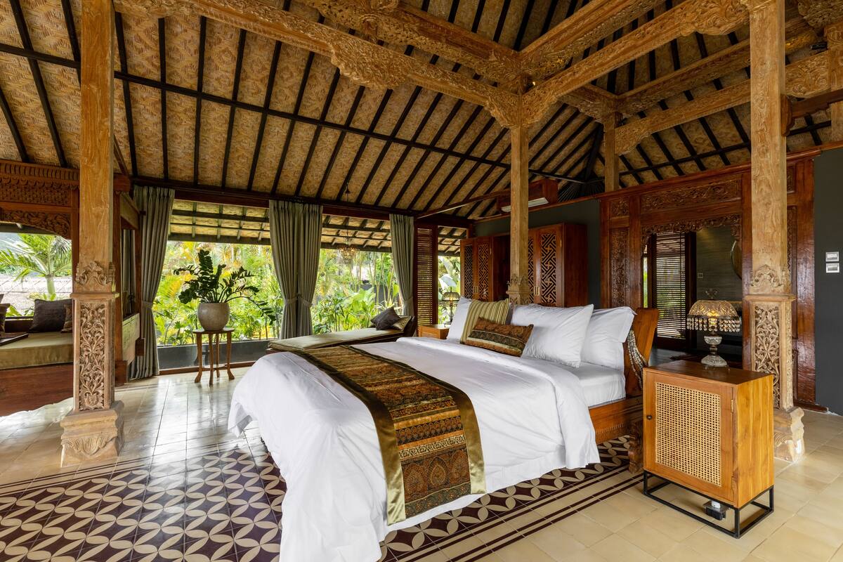 A spacious room with a large bed, a wooden cabinet, and a view of greenery outside.