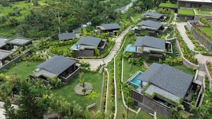 A modern resort with multiple bungalow-style buildings, a central swimming pool, and lush surrounding greenery.