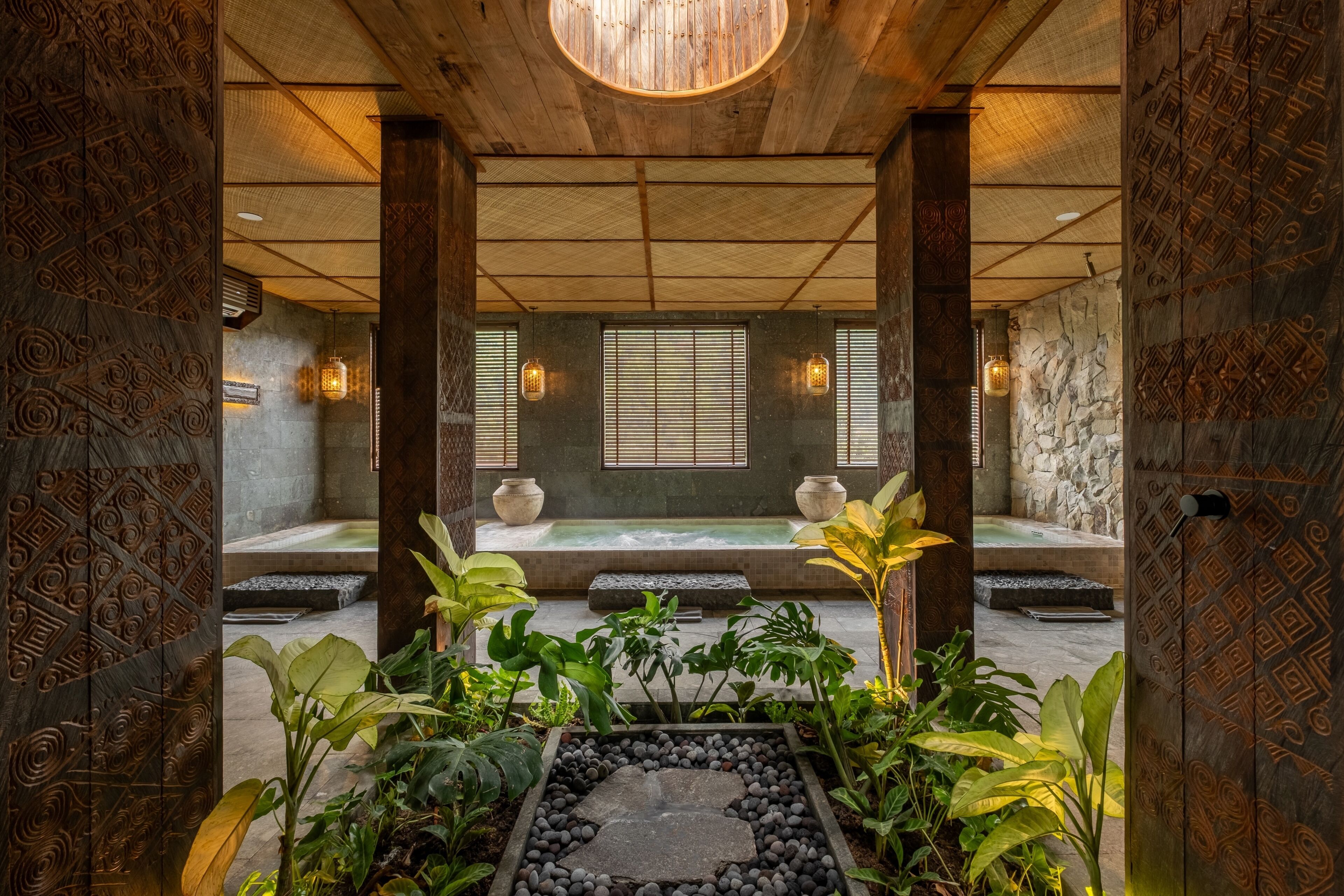 Un salón de spa tradicional con pared de piedra, techo de madera y un elemento central de agua.