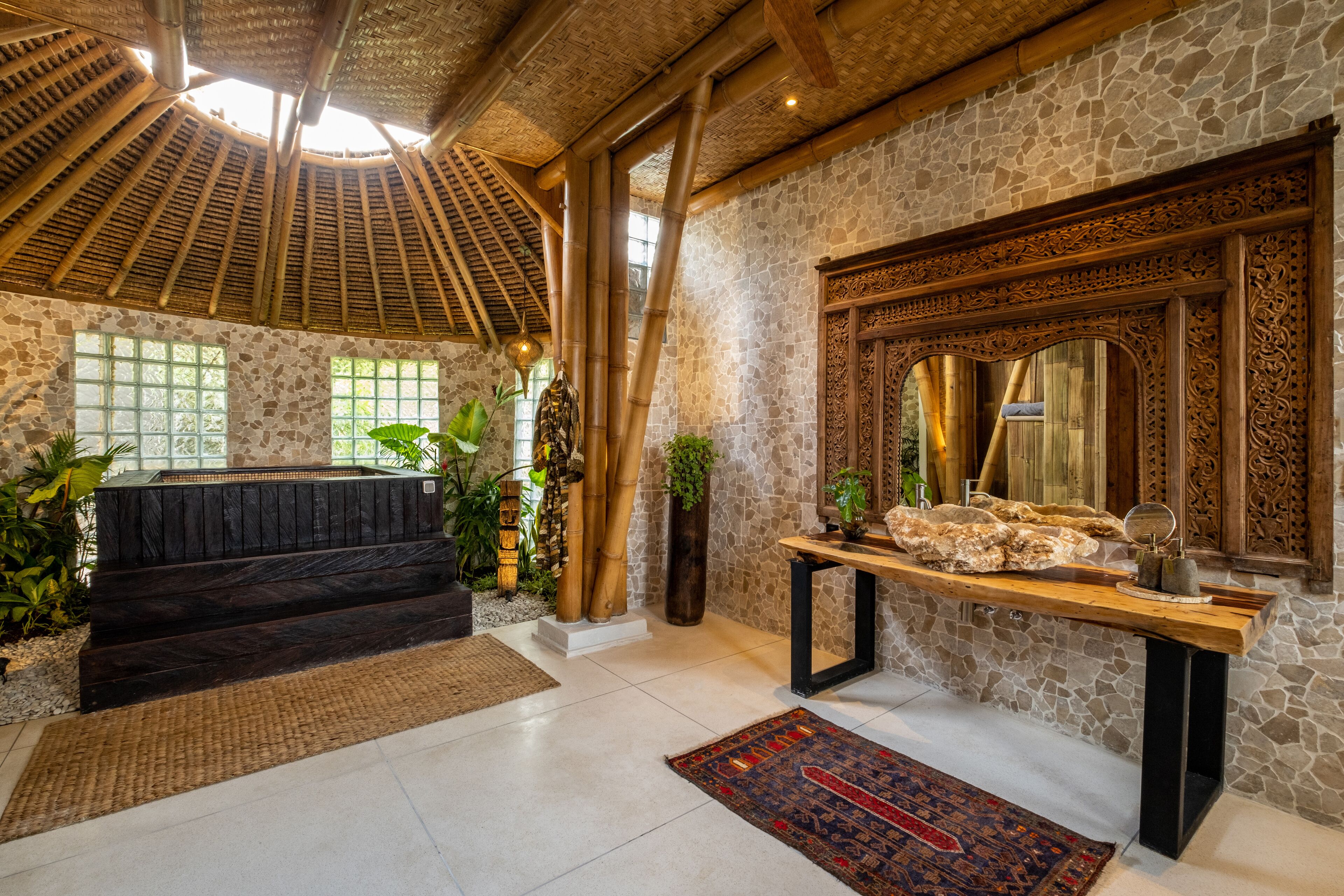 A spacious room with a stone wall, a wooden bench, a large mirror, and a wooden table with a vase.
