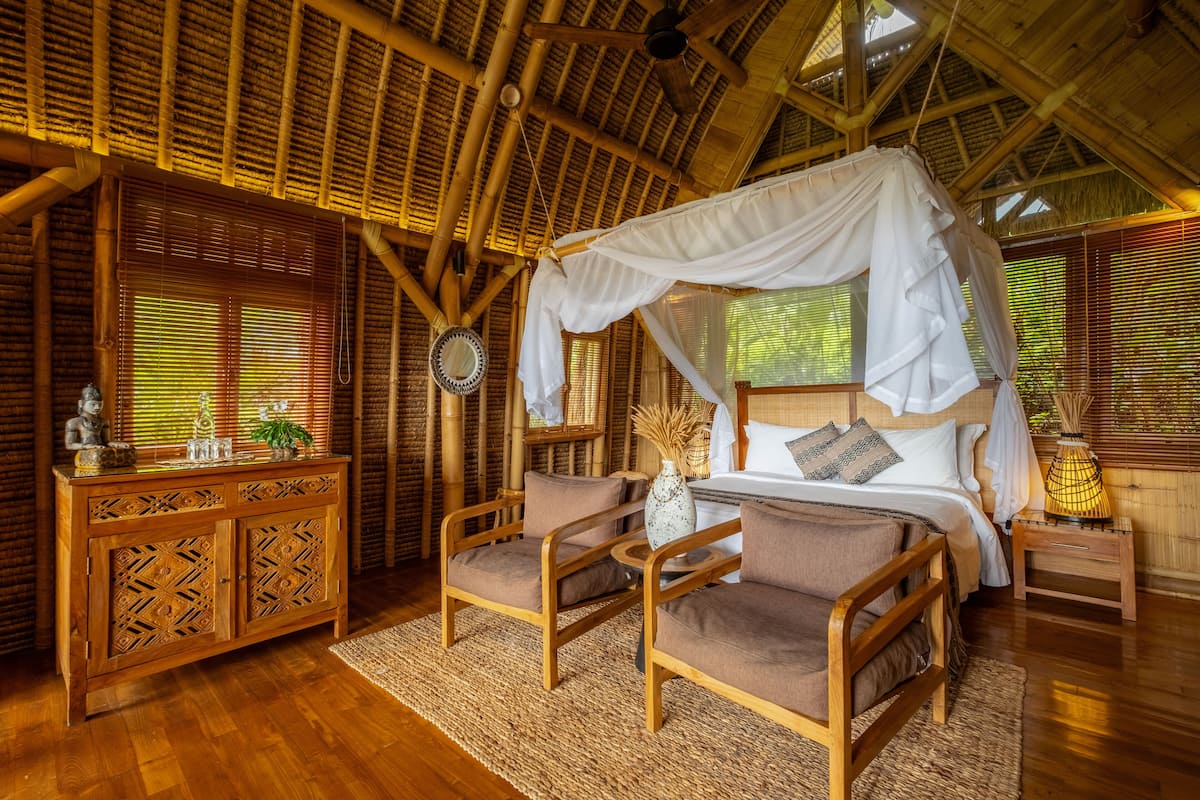 A room with a bed under a canopy, wooden furniture, and a large window with blinds.
