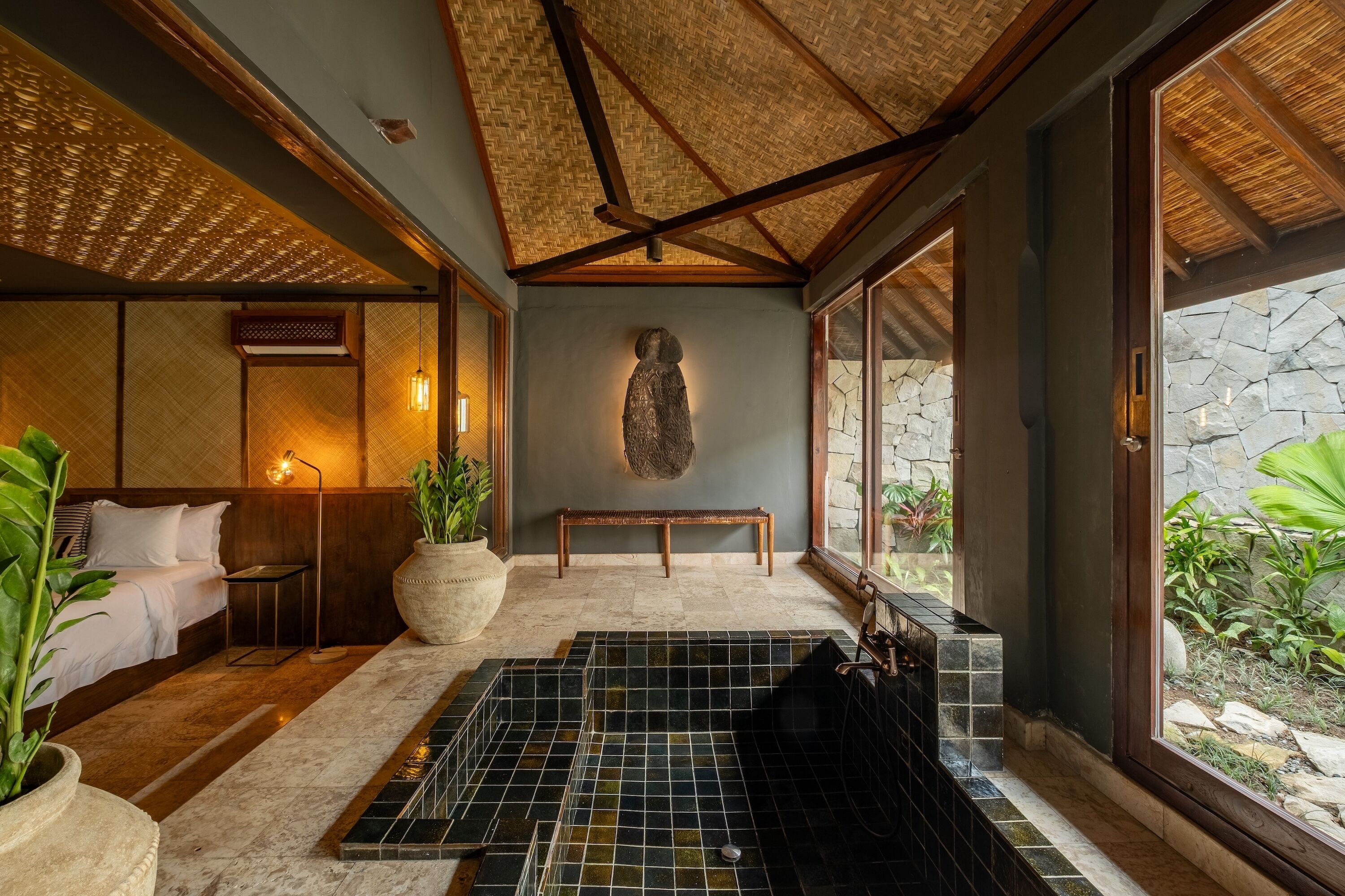 Un área de spa con pared de piedra, un banco de madera y una planta grande en maceta.