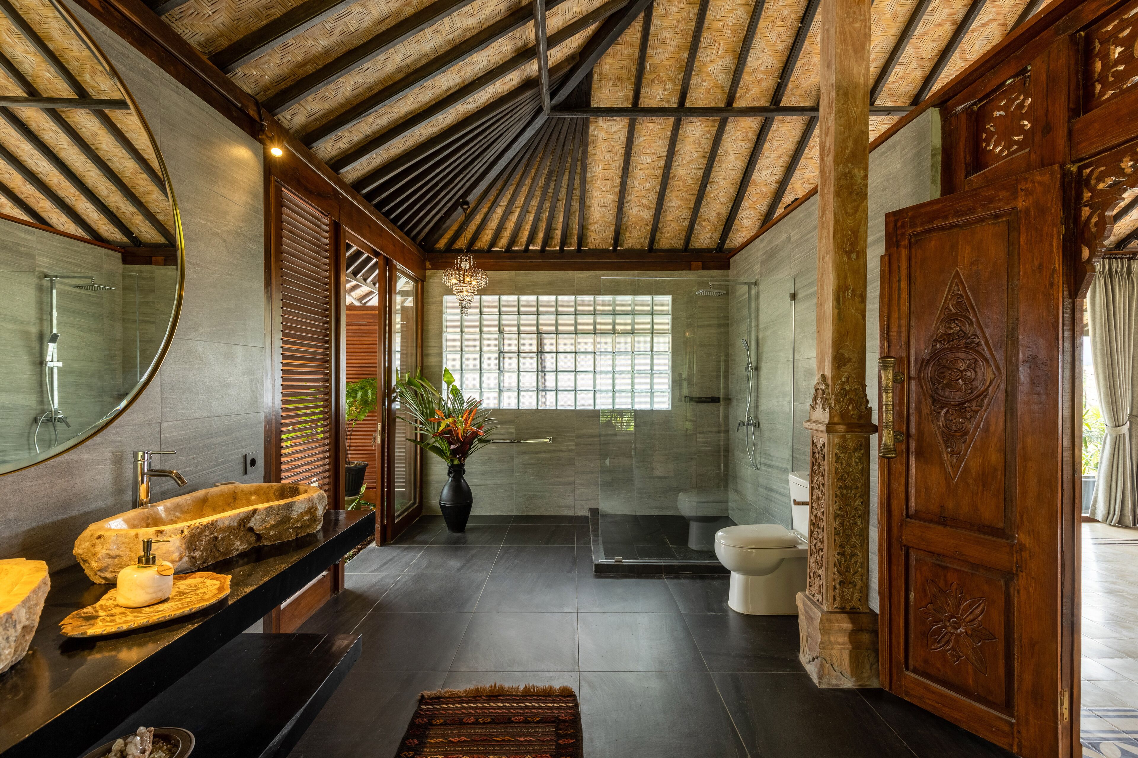 A modern bathroom with a large stone sink, a glass shower, and a wooden door.