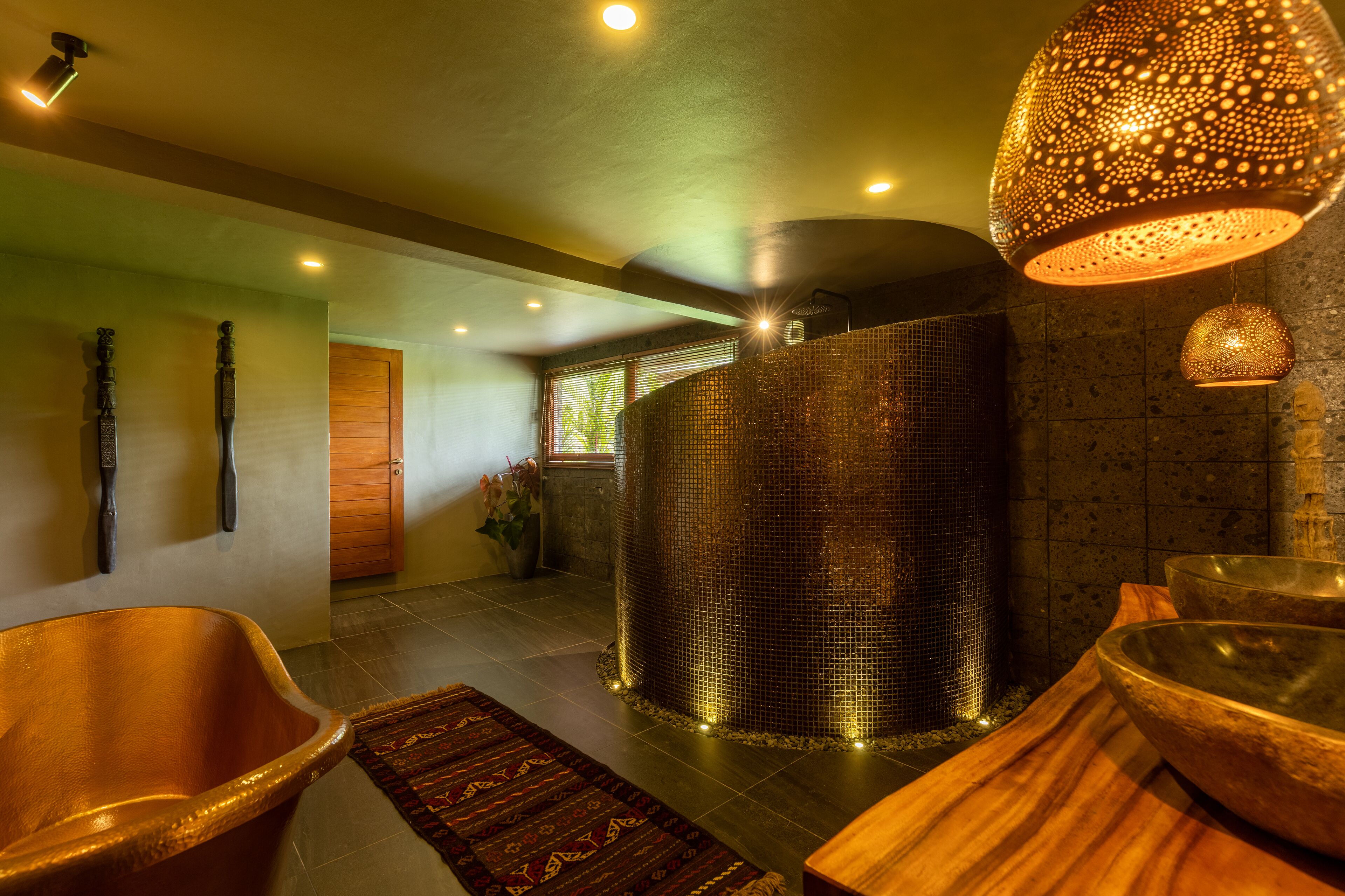 Un espace spa moderne doté d’une grande colonne à la texture particulière, d’un banc en bois et d’un tapis à motifs.