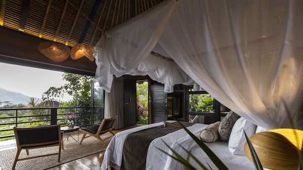 A bedroom with a large bed, a chair, and a view of the outdoors.