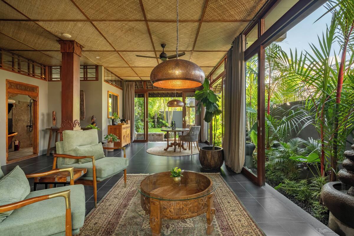 A spacious living area with a large window, a ceiling fan, and a round wooden coffee table.