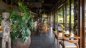 A spacious dining area with a long wooden table, wicker chairs, and hanging plants.