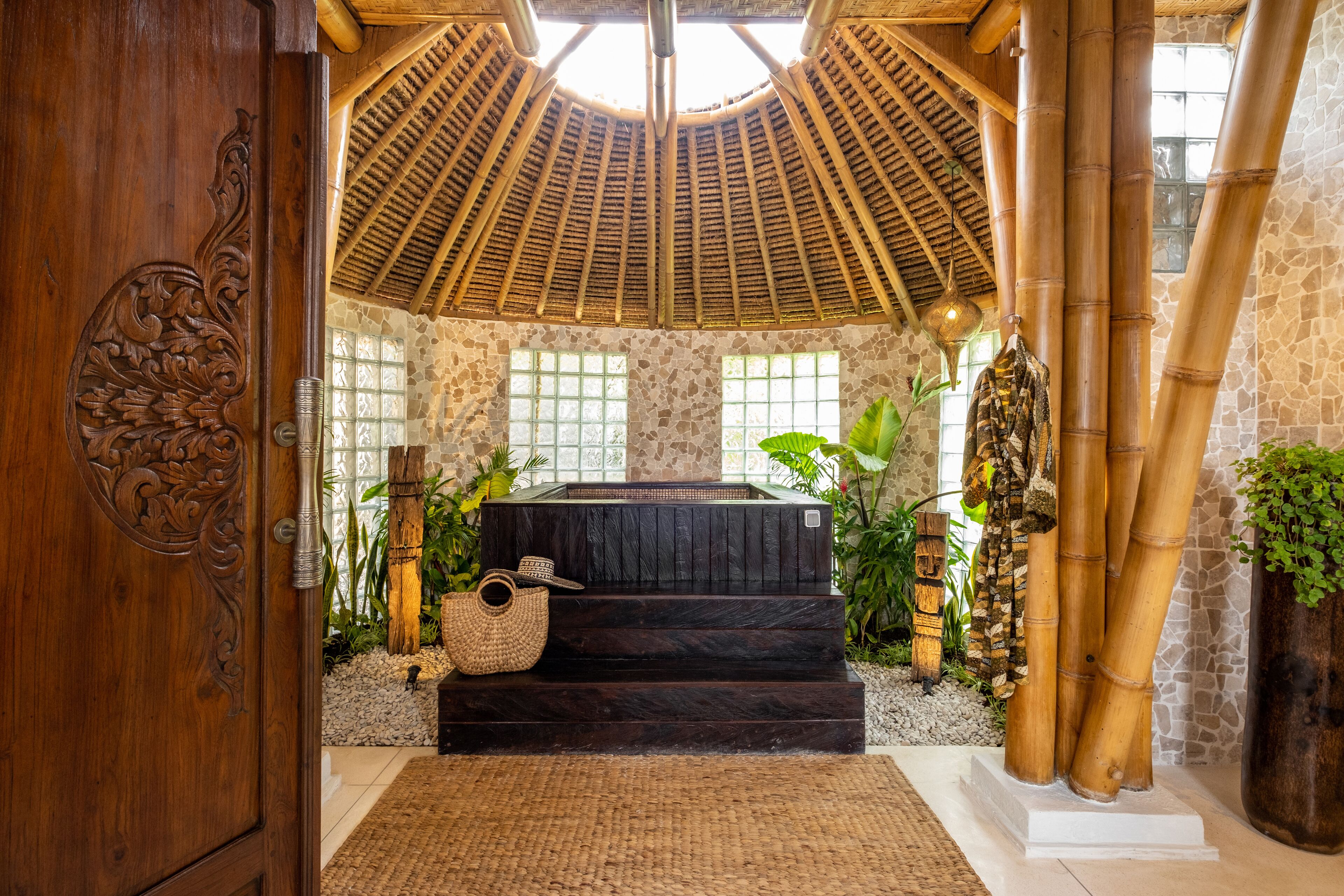 A spa area with a wooden door, a stone wall, a bamboo structure, and a hot tub.