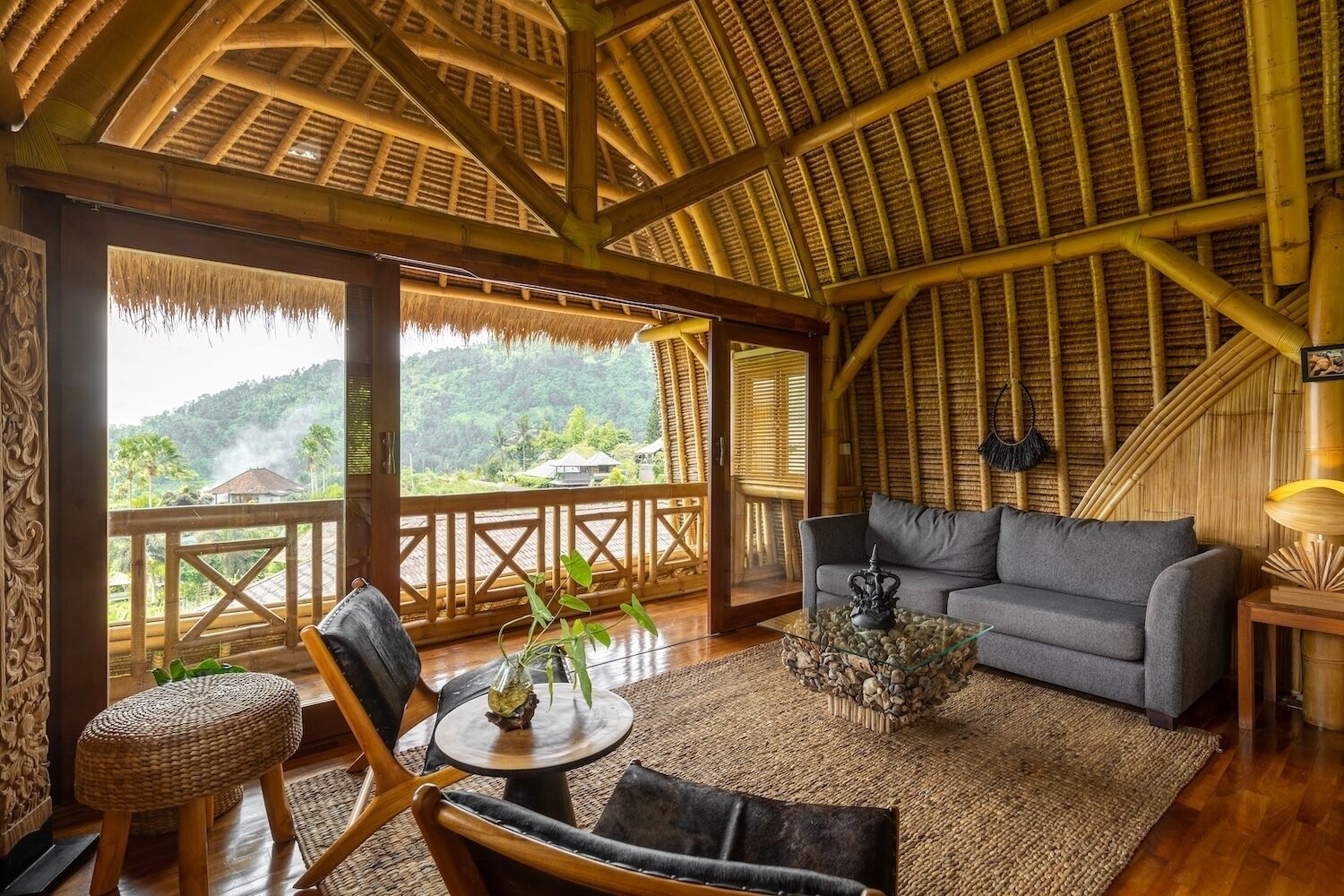 A room with a bamboo ceiling, a sofa, a coffee table, and a view of a lush landscape.