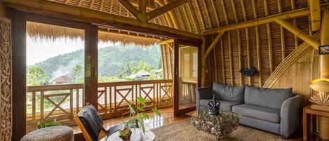 A room with a bamboo ceiling, a sofa, a coffee table, and a view of a lush landscape.