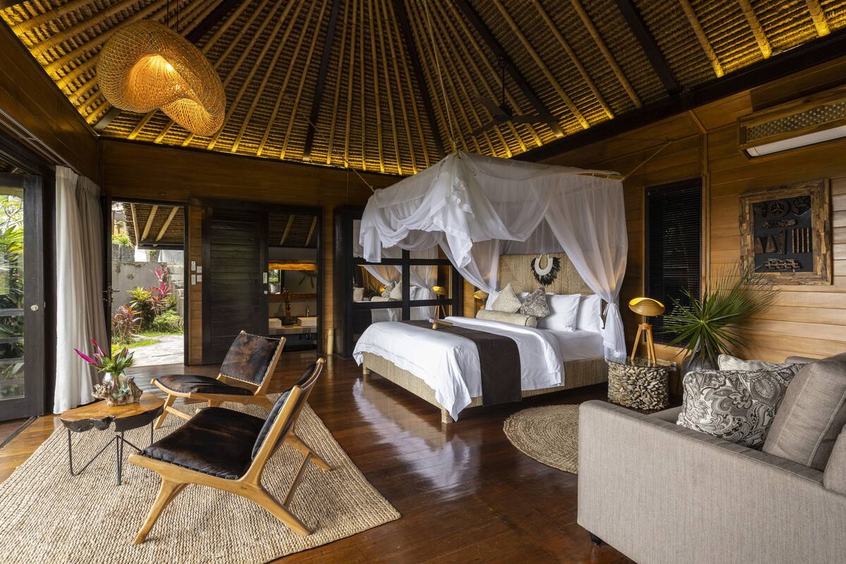 A spacious bedroom with a large bed, a sitting area with chairs, a dining table, and a view of the outdoors.