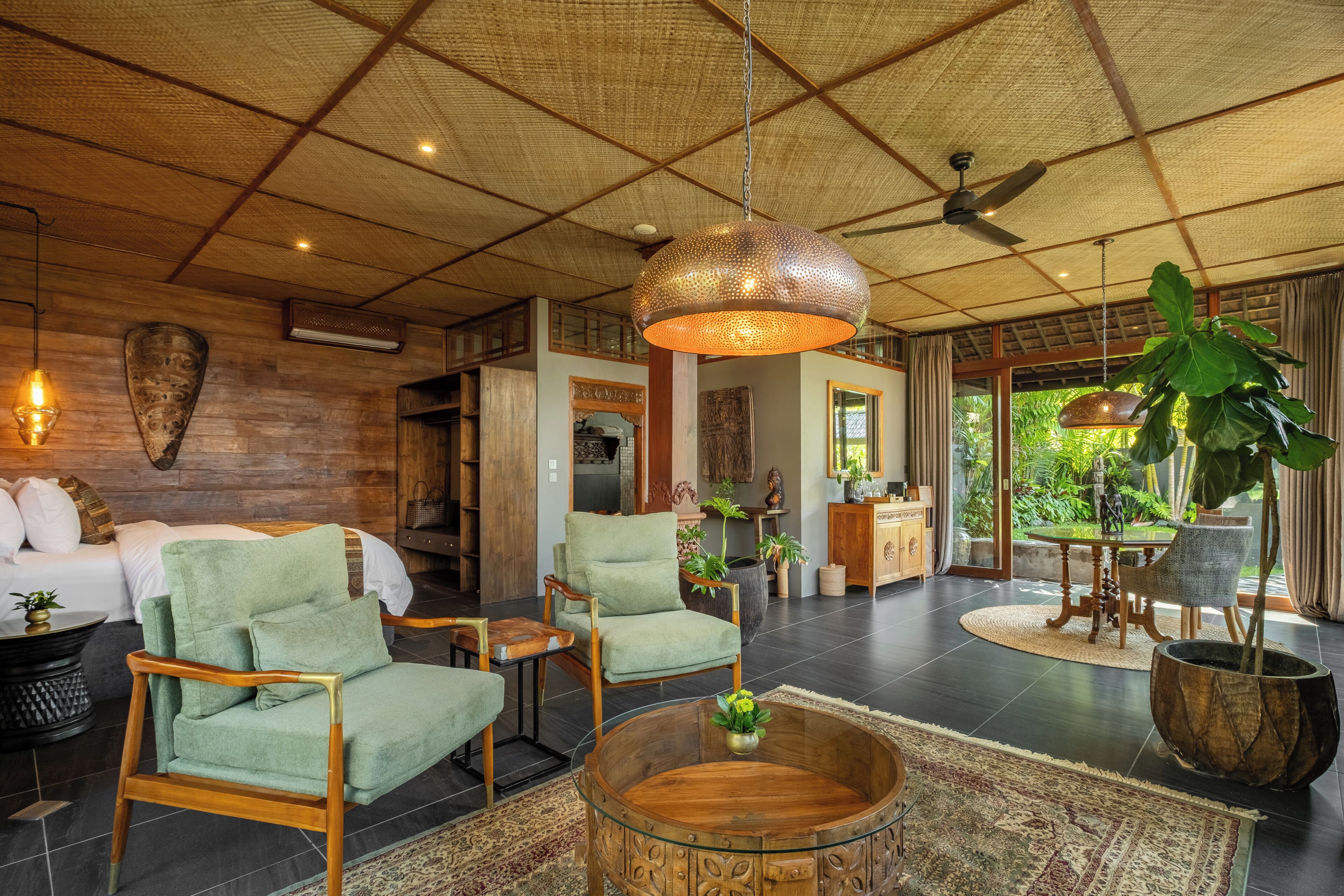 A spacious living area with a high ceiling, a ceiling fan, a large hanging light fixture, and a view of the outdoors.
