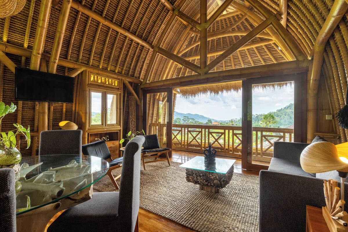 A room with a glass table, chairs, a television, and a view of the mountains.