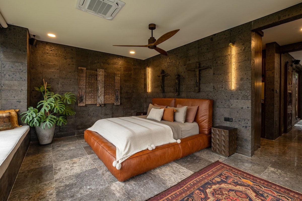 A bedroom with a large bed, a ceiling fan, and a potted plant.
