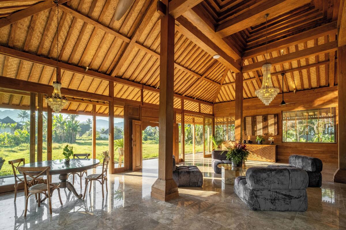 A spacious indoor area with a high ceiling, wooden beams, a round table with chairs, and a seating area with cushions.