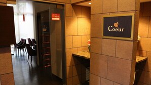 Um saguão de hotel com uma placa com a inscrição 'Cœur' e uma área de estar com cadeiras e uma mesa.