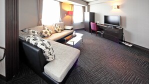 Quarto de hotel moderno com sofá, escrivaninha, televisão e uma grande janela com cortinas.