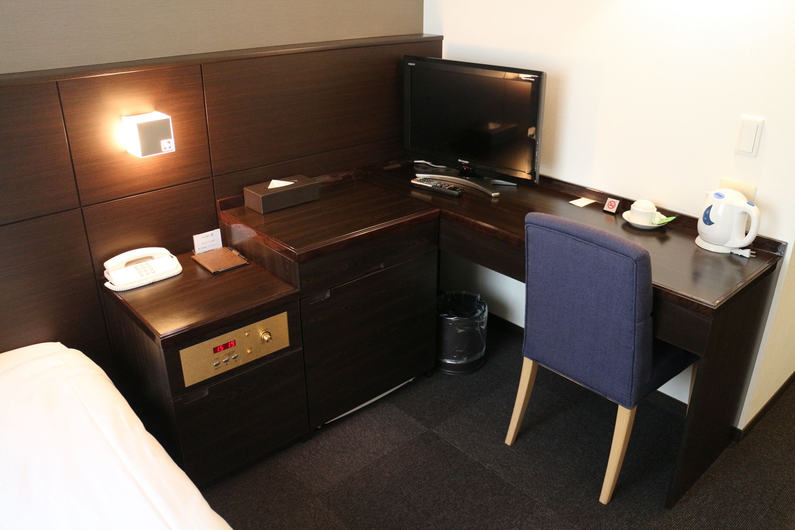 Une chambre d’hôtel comprenant un lit, un bureau avec une télévision, une chaise, une machine à café et une poubelle.
