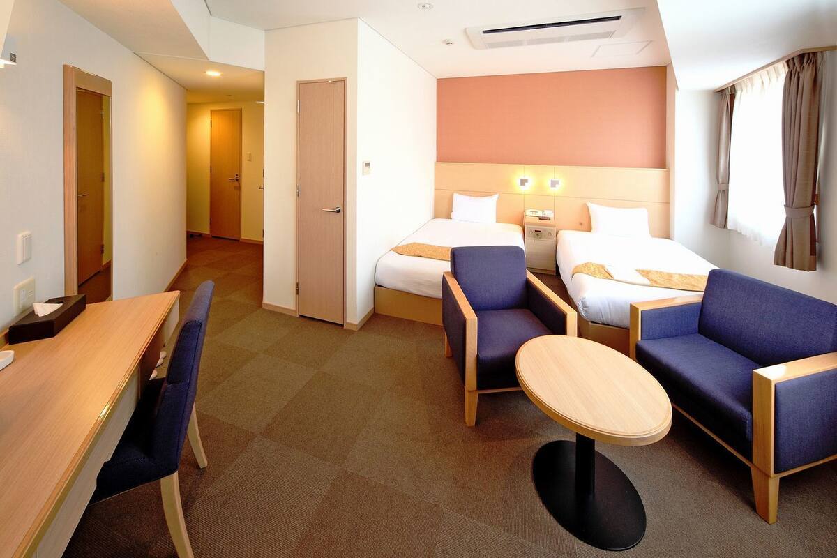 A hotel room with a bed, two sofas, a small table, and a desk.